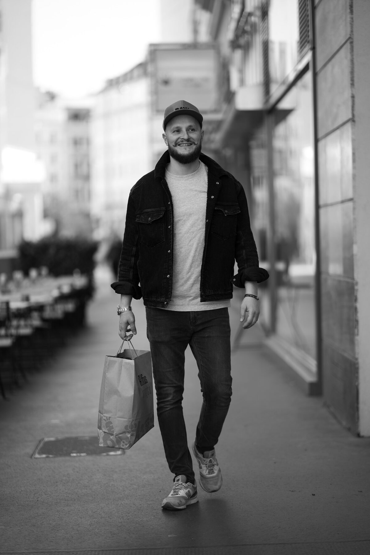 porträtfotograf Wien. Junger Mann mit Einkaufstasche spaziert entspannt durch die Wiener Innenstadt, aufgenommen vom Fotograf Wien in klassischem Schwarz-Weiß.