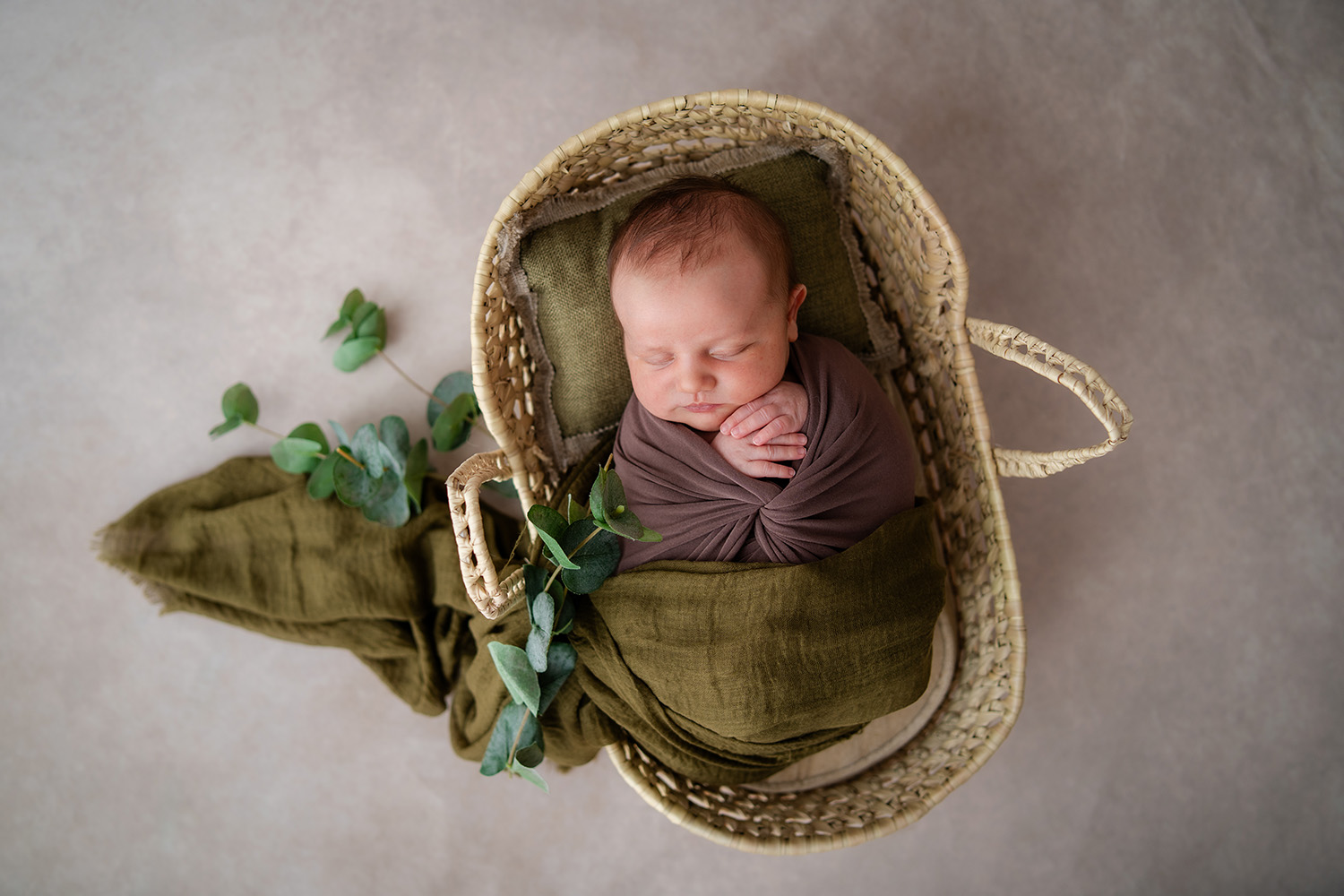 Neugeborenes Baby schläft friedlich im Korb – natürliches Babyshooting mit Eukalyptus in Wien.