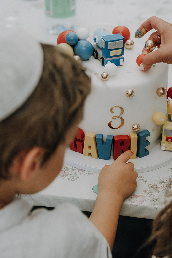 Kinder zeigen begeistert auf einen bunt dekorierten Geburtstagskuchen mit Zugmotiv, ein liebevoller Moment einer fröhlichen Feier, authentisch festgehalten von einem Familien Fotograf Wien beim Kindergeburtstag.