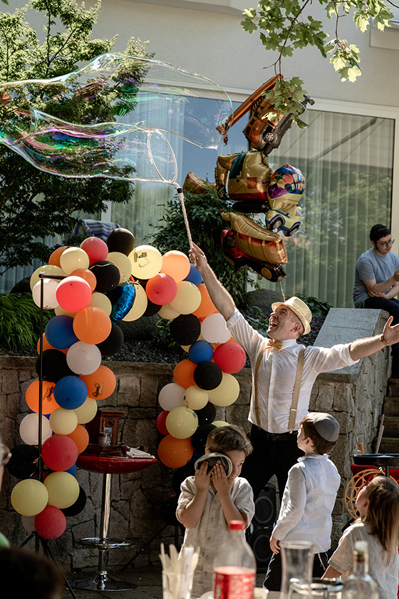Kinder beobachten begeistert einen Partyclown, der eine große Seifenblase bei einer fröhlichen Outdoor‑Geburtstagsfeier entstehen lässt, lebendig festgehalten von einem Kinderparty Fotograf Wien.