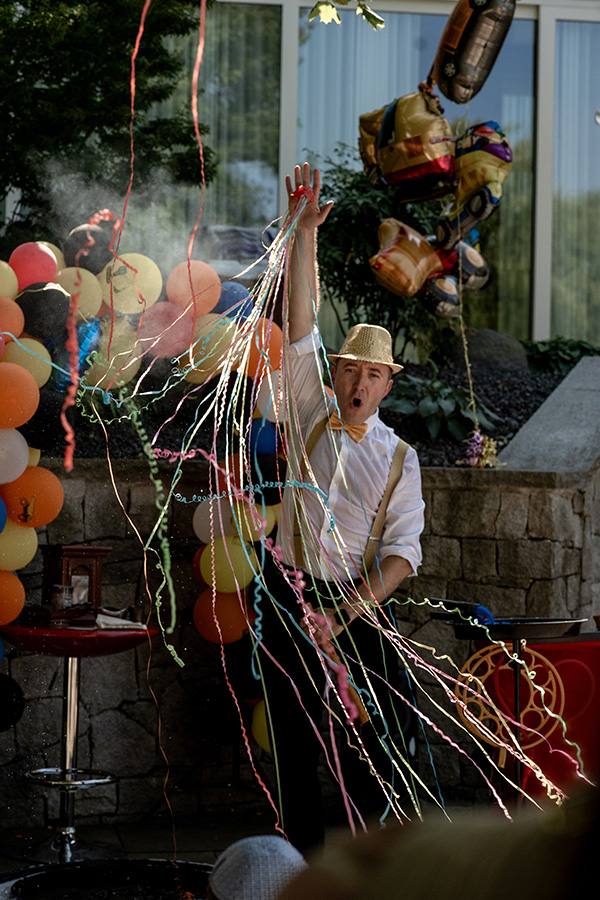 Partyclown wirft bunte Luftschlangen in die Luft und sorgt bei einer fröhlichen Outdoor‑Kinderparty für Begeisterung, lebendig festgehalten von einem Kinderparty Fotograf Wien.