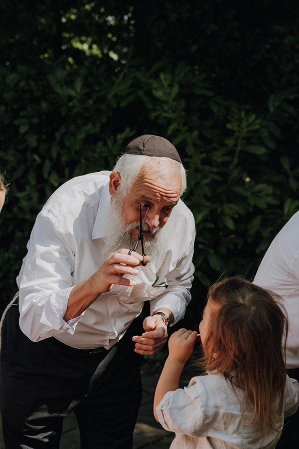 Älterer Mann interagiert liebevoll mit einem kleinen Kind im Grünen, ein ruhiger familiärer Moment, authentisch festgehalten von einem Fotograf Wien und Familienfotograf.