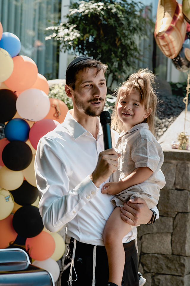 Vater hält sein lachendes Kind während einer jüdischen Geburtstagsfeier vor einer farbenfrohen Ballonwand, authentisch festgehalten von einem Kinderparty Fotograf Wien.