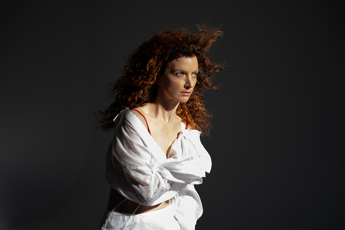 Stilvolles Portrait einer Frau mit roten Locken in weißer Bluse vor dunklem Hintergrund bei gerichteter Lichtsetzung