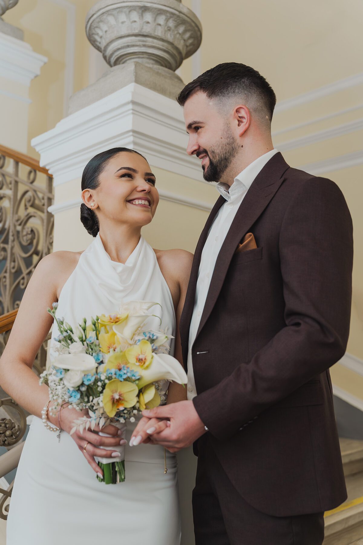 Brautpaar Portrait bei einer eleganten Hochzeit im Innenraum, das Paar schaut sich lächelnd an und hält den Brautstrauß in den Händen. Hochzeitsfotografie von Shira Rachel.