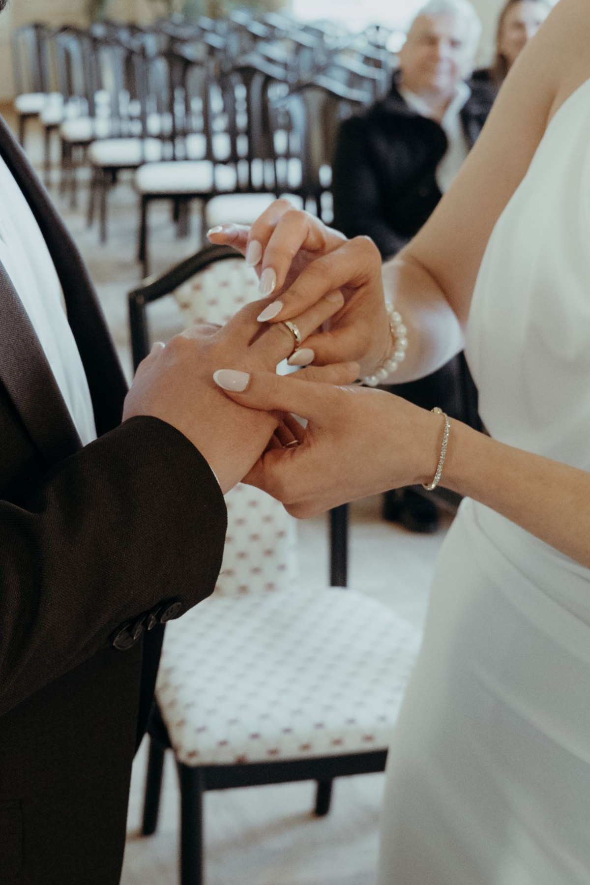 Nahaufnahme vom Ringtausch bei einer Standesamthochzeit, während die Braut dem Bräutigam den Ehering ansteckt.