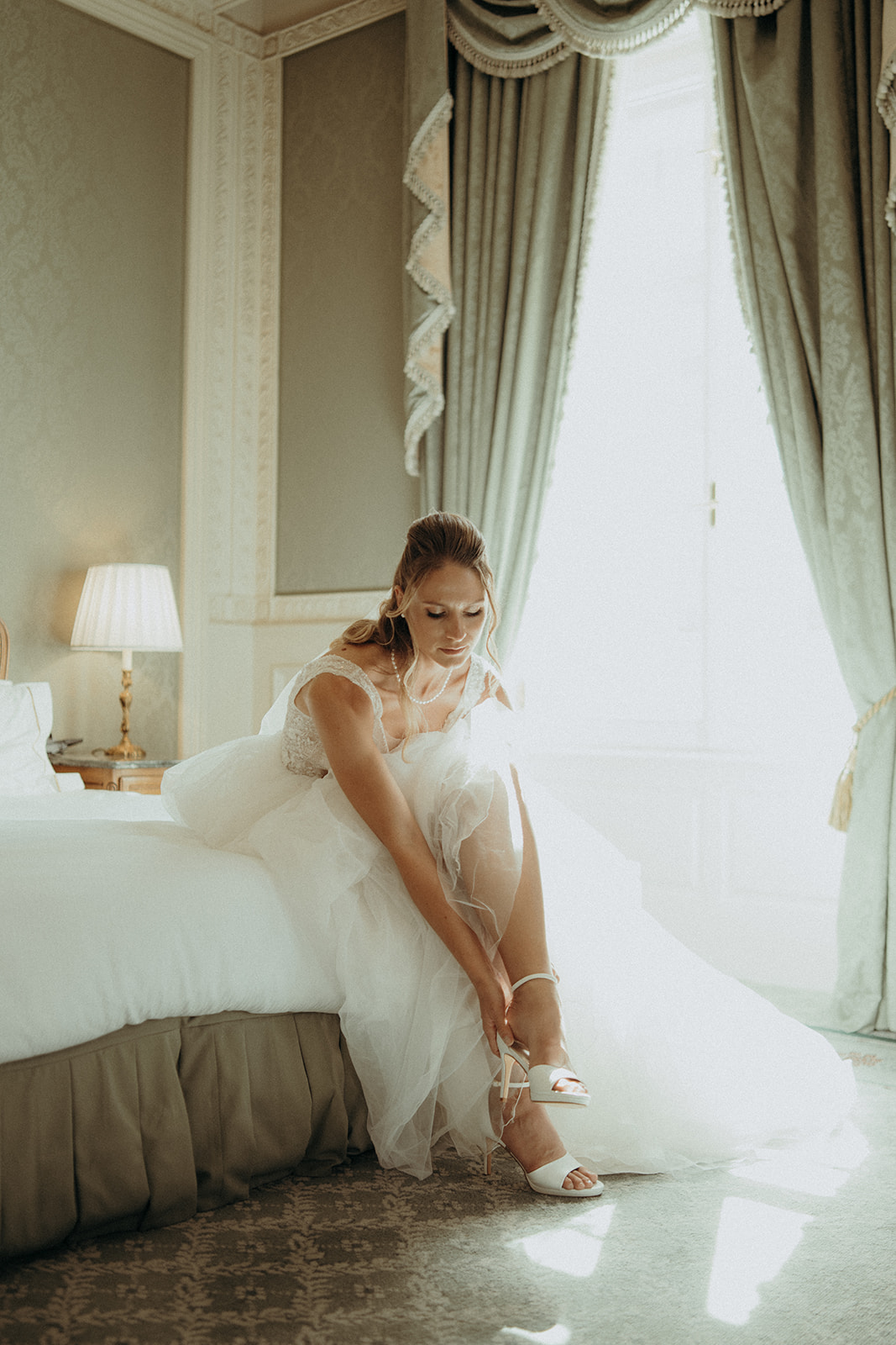 Braut im Grand Hotel Wien zieht ihre Hochzeitsschuhe an – stilvolle, natürliche Hochzeitsfotografie in Wien.